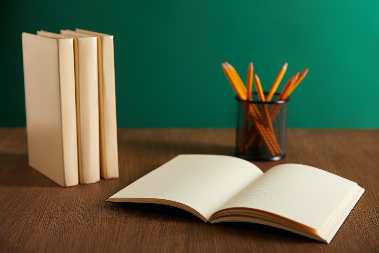 open textbook, books and pencils on wooden table